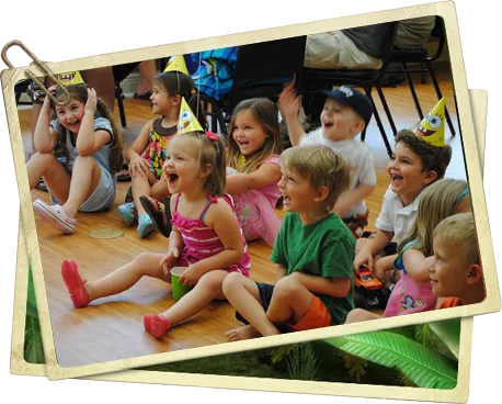 Children in birthday party hats clapping and cheering on a wooden floor